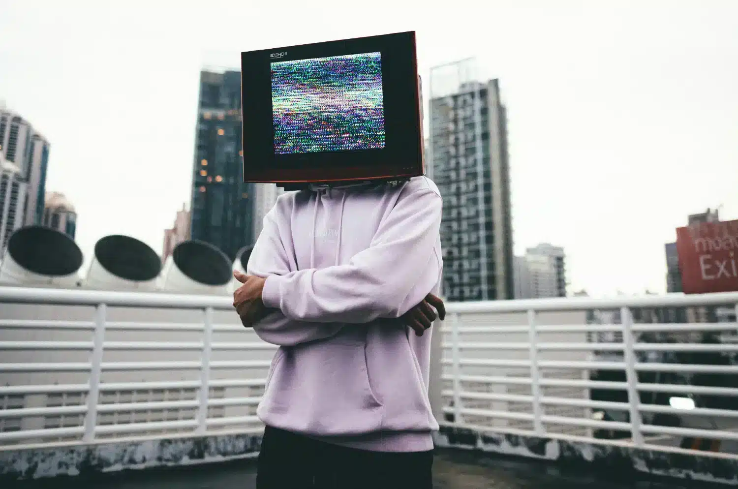 Photo of a man on a rooftop wearing a computer monitor on his head displaying static