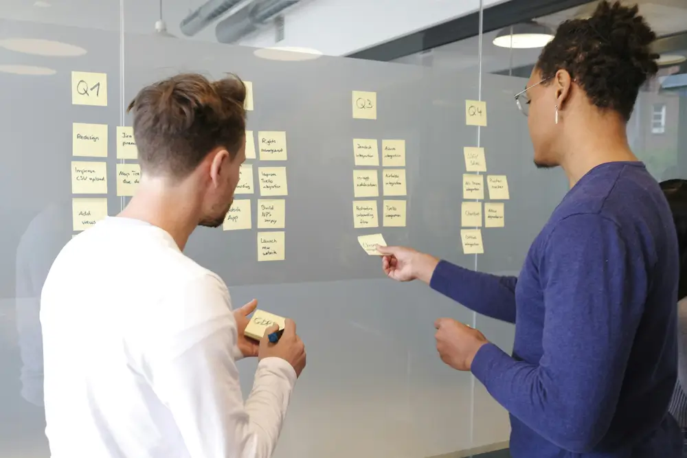 Two people putting sticky notes on a glass wall